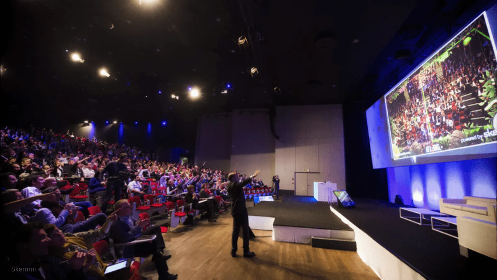 Large audience in an auditorium actively participating in a Skemmi interactive crowd game displayed on a big screen